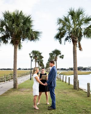 A romantic scene unfolds beneath palm trees along a coastal walkway at sunset.