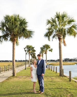 A couple stands on a palm tree-lined pathway along the waterfront at sunset in Charleston, South Carolina.