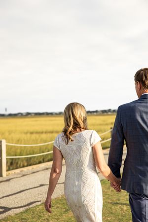 Couple walking hand in hand along a wooden boardwalk through golden marshland at sunset.