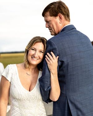 A couple in wedding attire shares an intimate moment during an outdoor photo session in a field.
