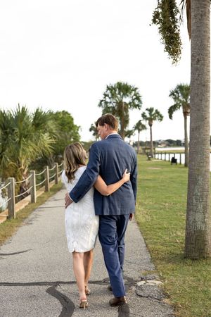 A couple walks together on a palm tree-lined path near the beach on a sunny day.