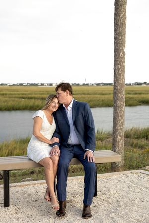 A couple shares an intimate moment on a bench by the water surrounded by palm trees and marsh grass.