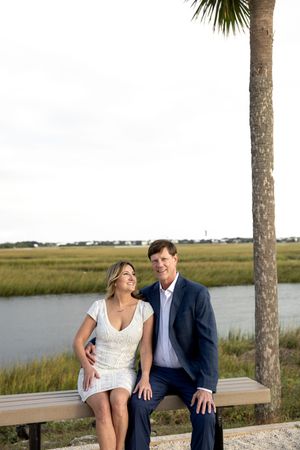 A couple sits together on a wooden bench overlooking a coastal marsh with palm trees in South Carolina.