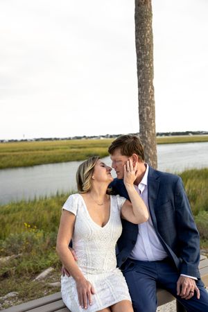 Romantic couple shares intimate moments on a bench by the marsh during sunset.