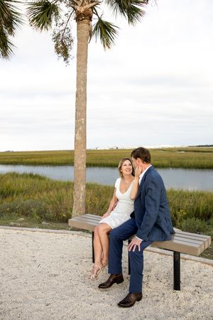 A couple shares a romantic moment sitting on a wooden bench overlooking a coastal marsh landscape.