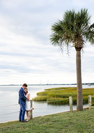 A couple embraces by a palm tree with scenic marshland and water views in the background.
