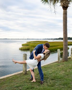 A romantic dip pose by a waterfront with a palm tree and marsh grasses in the background.