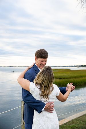 A couple embraces on a wooden dock by the marsh during a romantic sunset photoshoot.