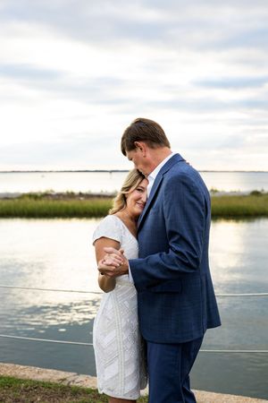 A couple shares an intimate dance pose on a dock overlooking a serene coastal waterway.