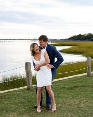 A couple shares an intimate moment near a wooden fence with coastal wetlands stretching behind them.