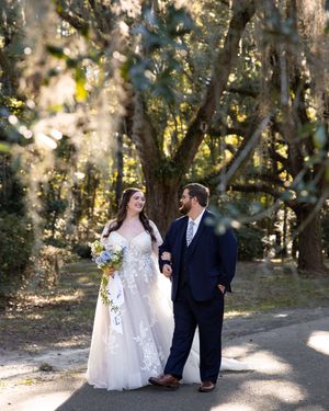 Romantic wedding couple poses in dappled sunlight beneath tree canopy.