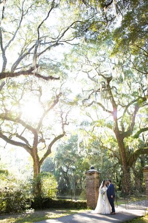 Couple embracing under sunlit oak trees with Spanish moss in a romantic garden setting.