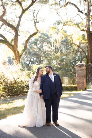 A couple shares a romantic moment on a tree-lined pathway during their wedding photoshoot.
