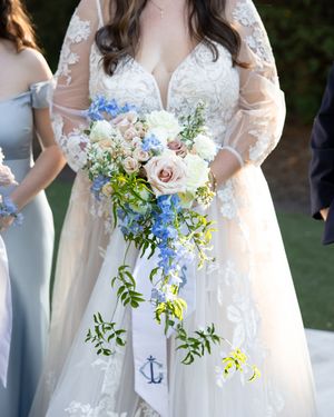 Wedding bouquet with cascading blue delphinium flowers, pink roses and greenery against white lace dress.
