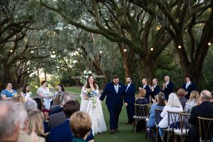 Guests mingle and celebrate at an elegant outdoor garden wedding reception under tall trees at dusk.