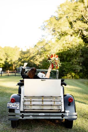 A vintage white car with a bouquet held up from the back seat on a sunny autumn day.