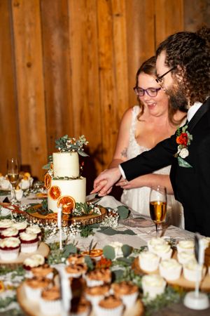 A wedding dessert table with a white tiered cake and cupcakes decorated with greenery and floral accents.