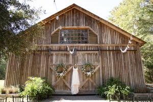 Rustic wooden barn decorated with wreaths and antlers features a white dress hanging between the double doors.