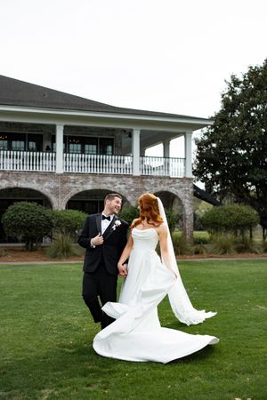 A couple in wedding attire share a romantic moment on a manicured lawn in front of a stately venue.