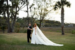 A romantic wedding couple poses together in a scenic outdoor setting with palm trees and natural landscape.