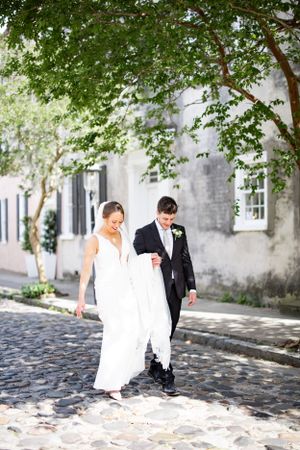 Couple in wedding attire strolling on a historic cobblestone street in Charleston.