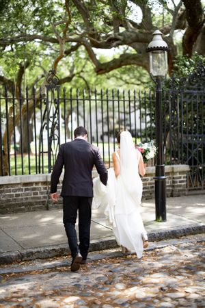 Newlyweds walking along a charming brick path with wrought iron gate and Spanish moss draped trees overhead.
