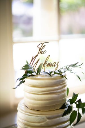 Elegant white wedding cake with greenery and custom topper decoration.