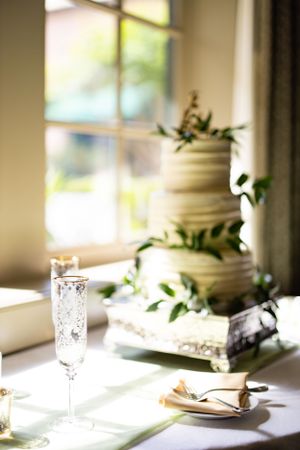 A sunlit white tiered wedding cake decorated with fresh green foliage.