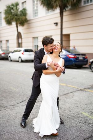 A joyful wedding couple sharing a romantic moment on a palm tree lined street.