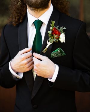 Elegant groom's attire featuring black tuxedo, emerald tie and red rose boutonniere.