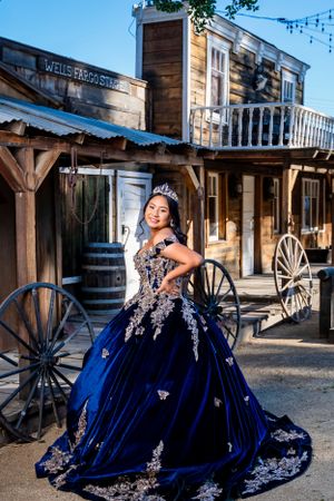 A stunning royal blue velvet ballgown with silver embellishments photographed against a rustic western storefront backdrop.
