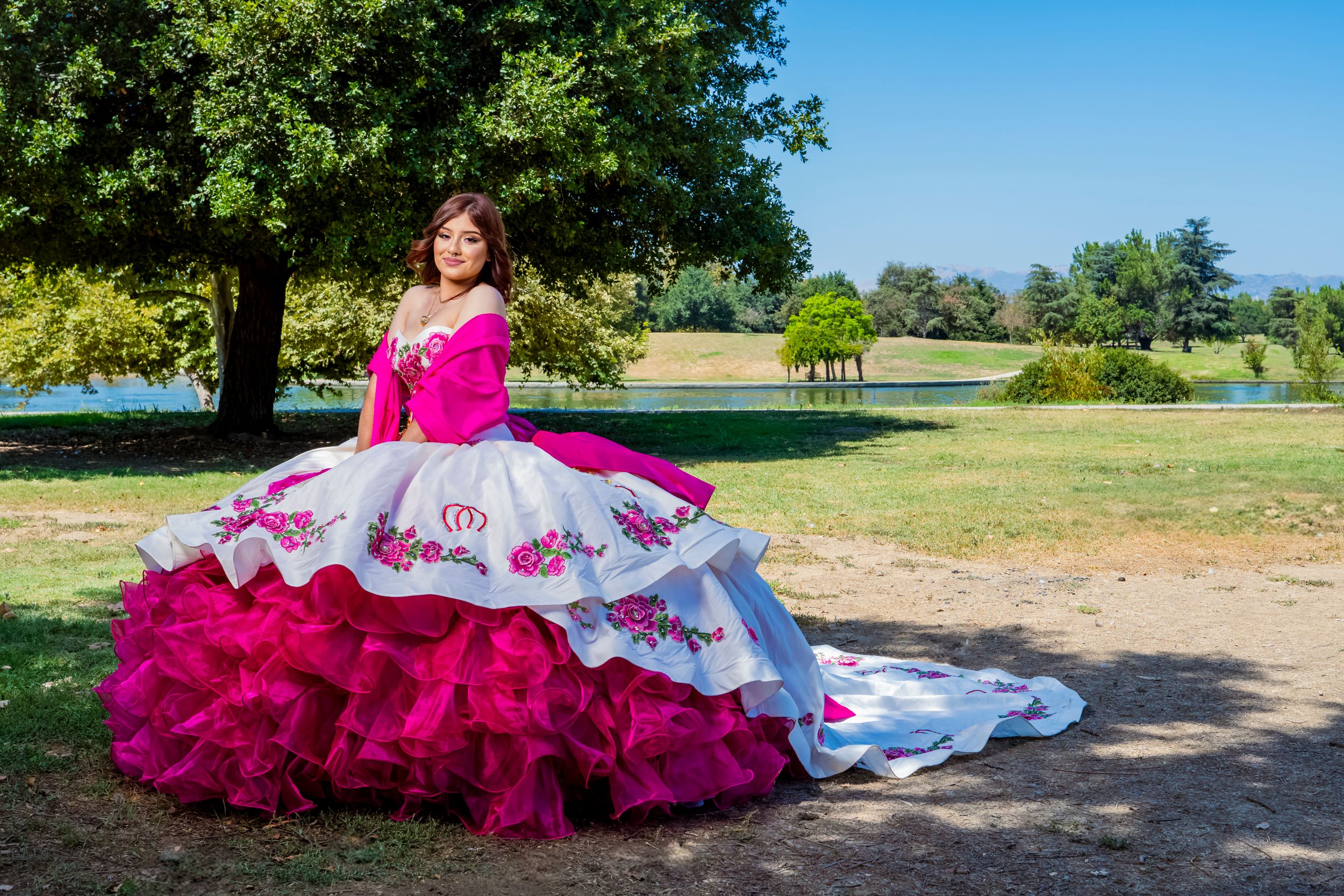 Stunning quinceañera dress in fuchsia and white with elaborate ruffles in outdoor garden setting.