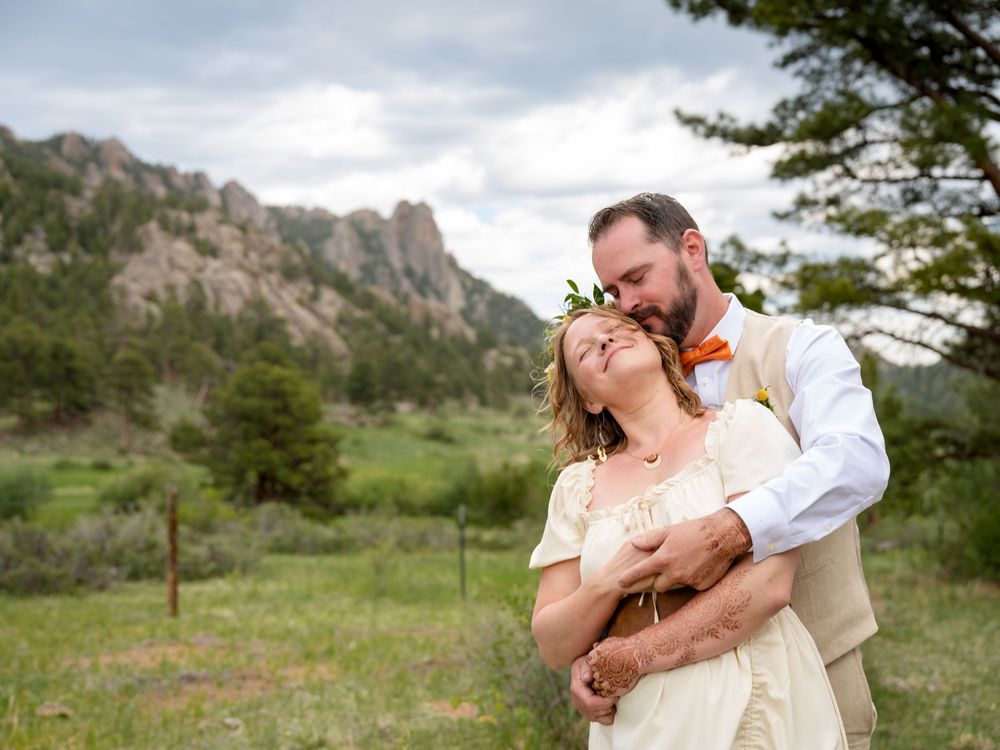 Couple embracing in a meadow with rocky mountain backdrop during outdoor wedding ceremony in Colorado.