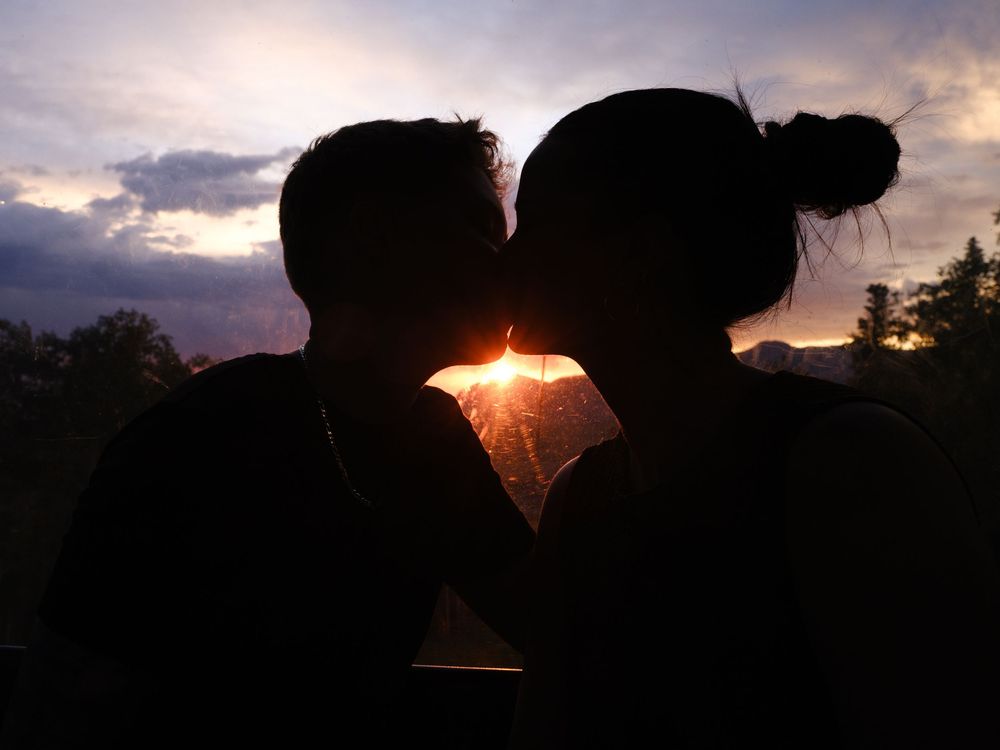 Silhouetted couple sharing a kiss at sunset with sunlight peeking through between them.