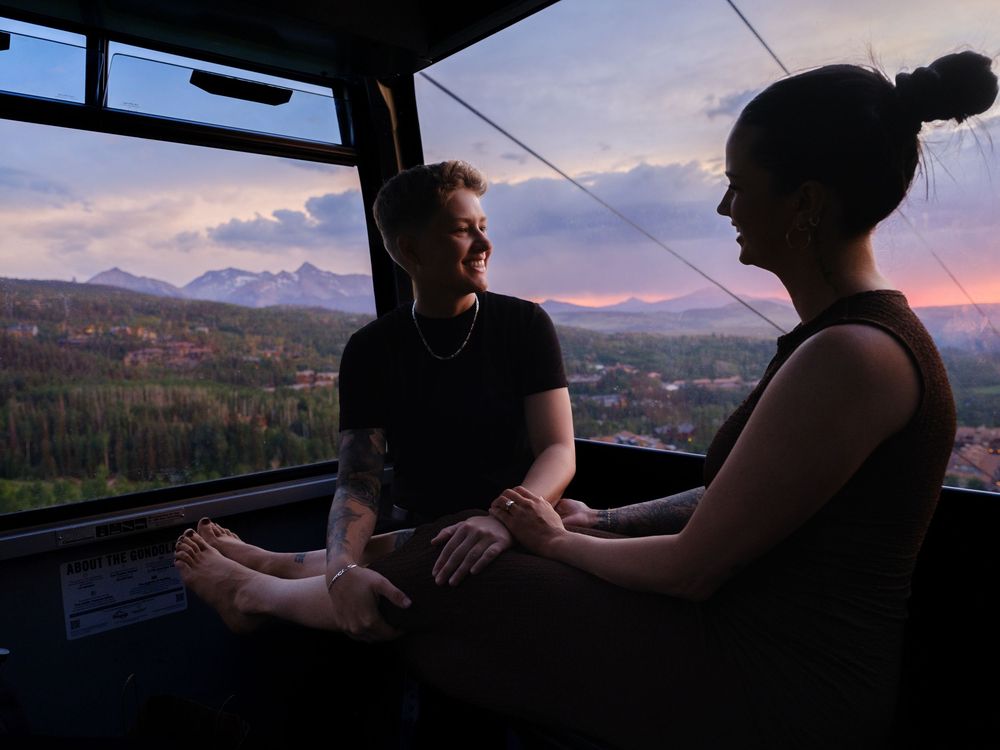 Two silhouettes in conversation inside a cable car against a scenic mountain sunset backdrop.