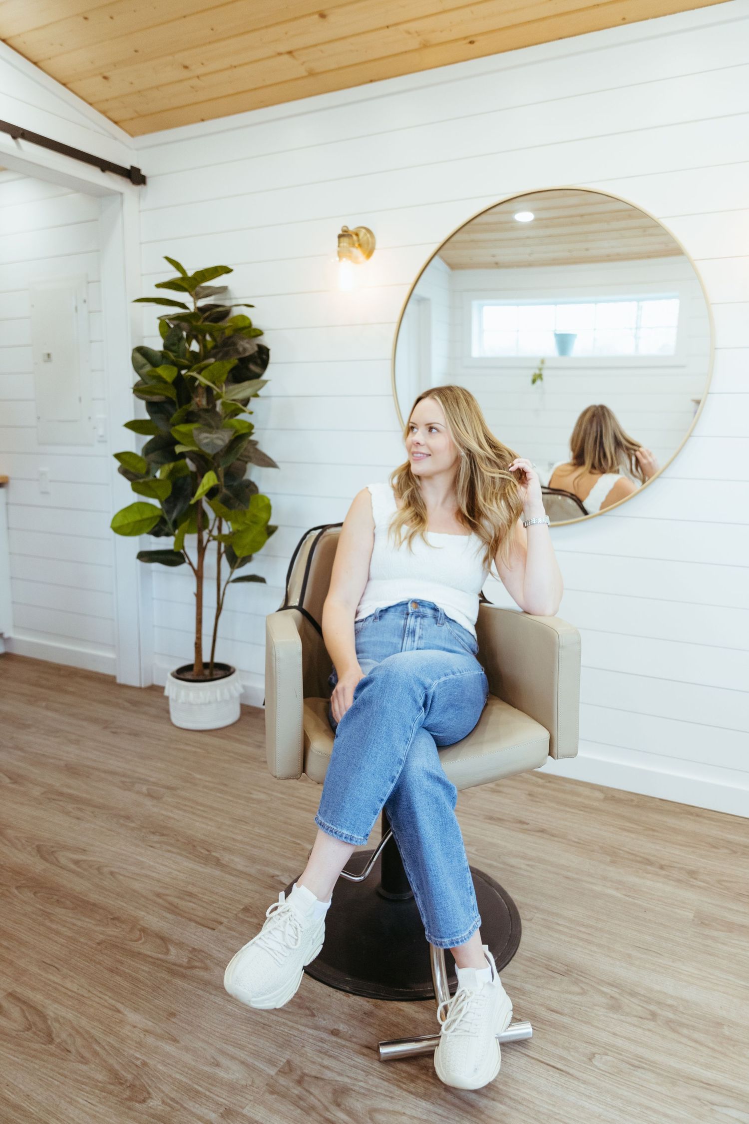 Modern minimalist interior with round mirror, white walls, wooden floor, potted fiddle leaf fig plant and white sneakers.