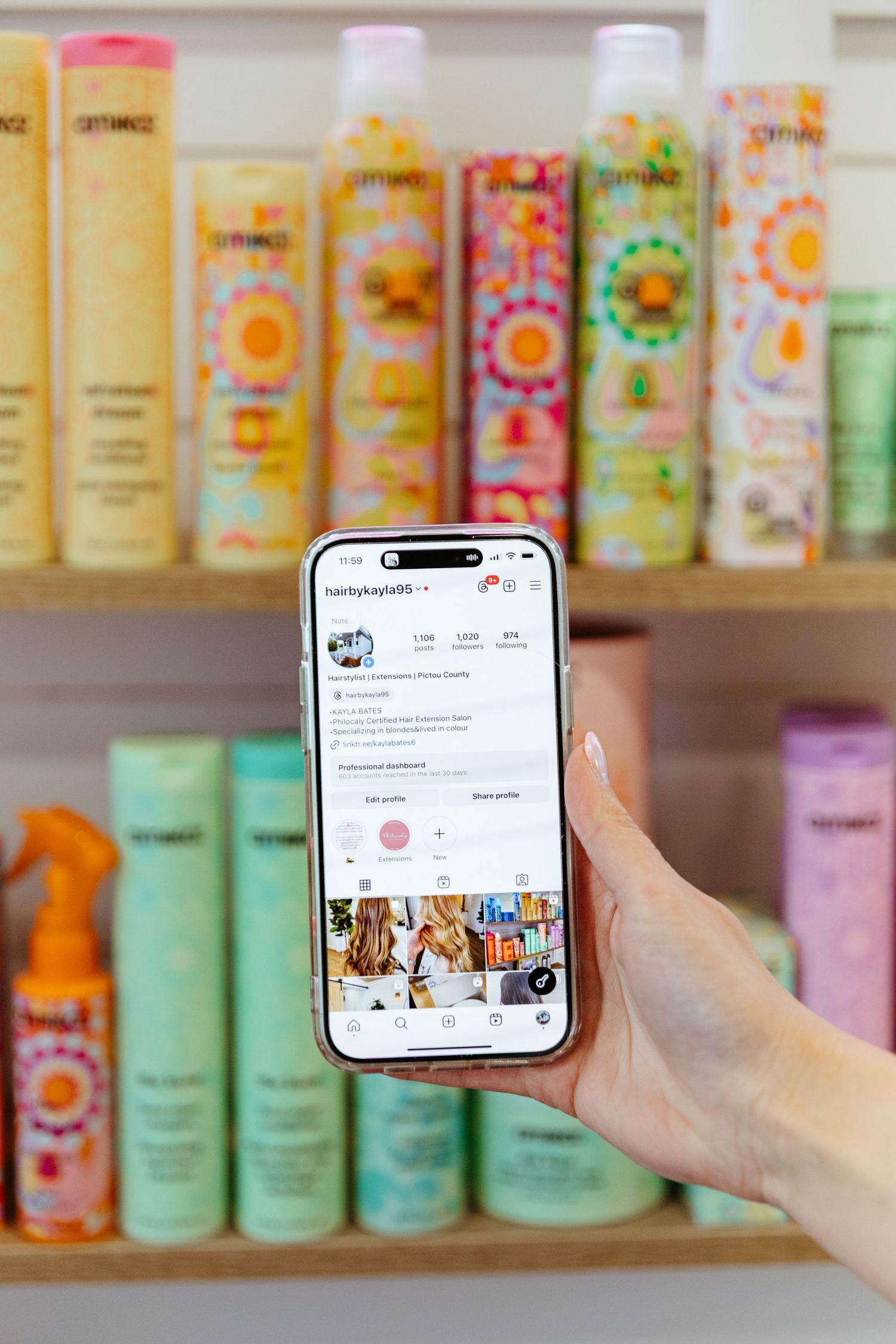 Hand holding phone displaying social media app against backdrop of colorful haircare products on store shelves.