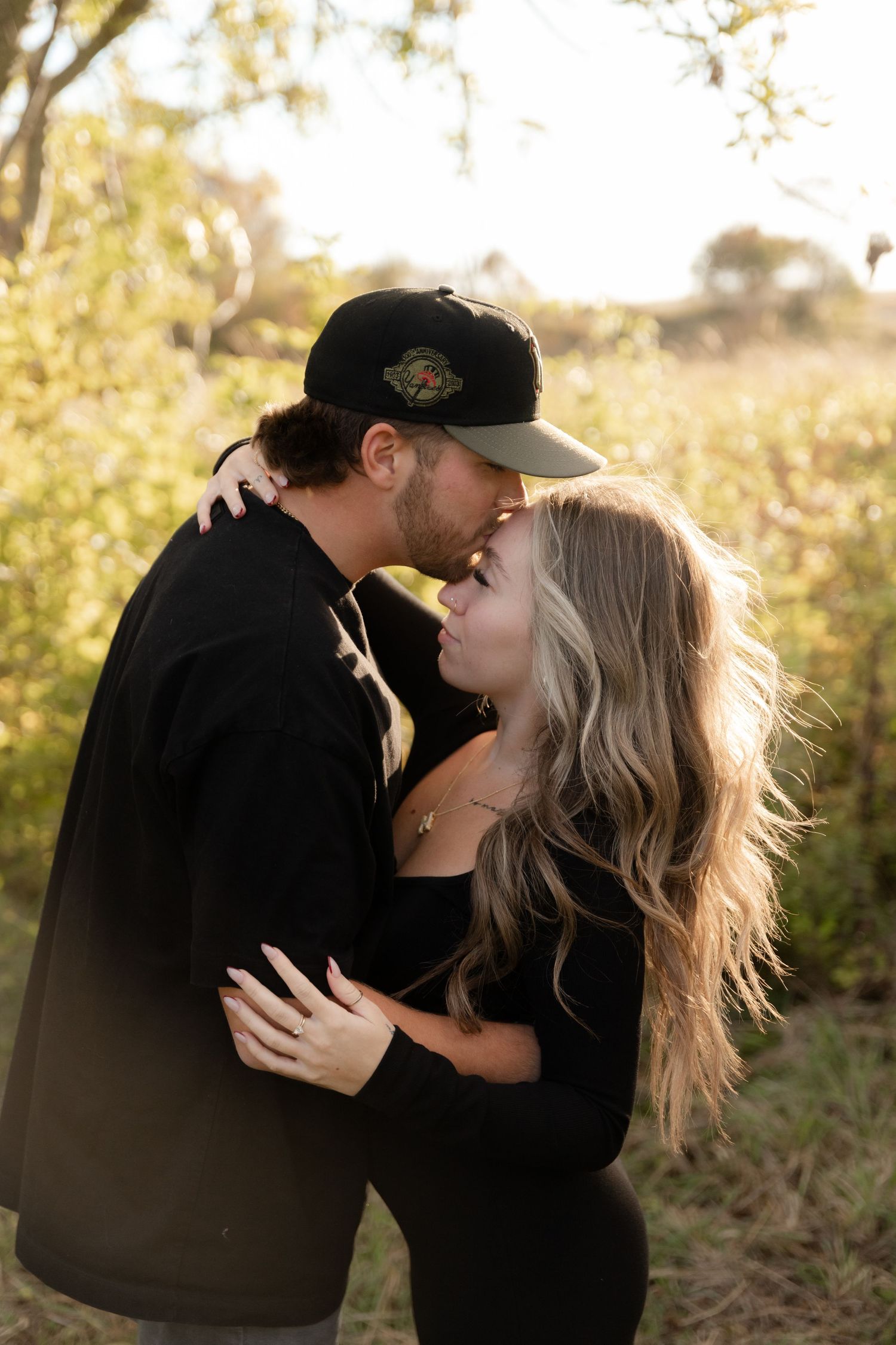 A romantic couple embraces in golden sunlight during an outdoor photo session.