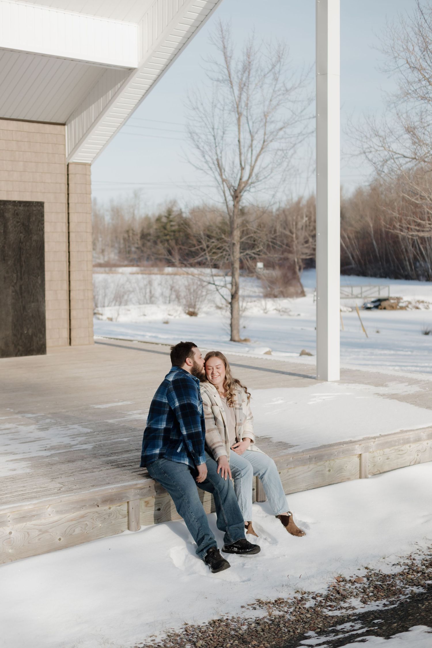 A couple sits together on concrete steps outside a building on a snowy winter day.