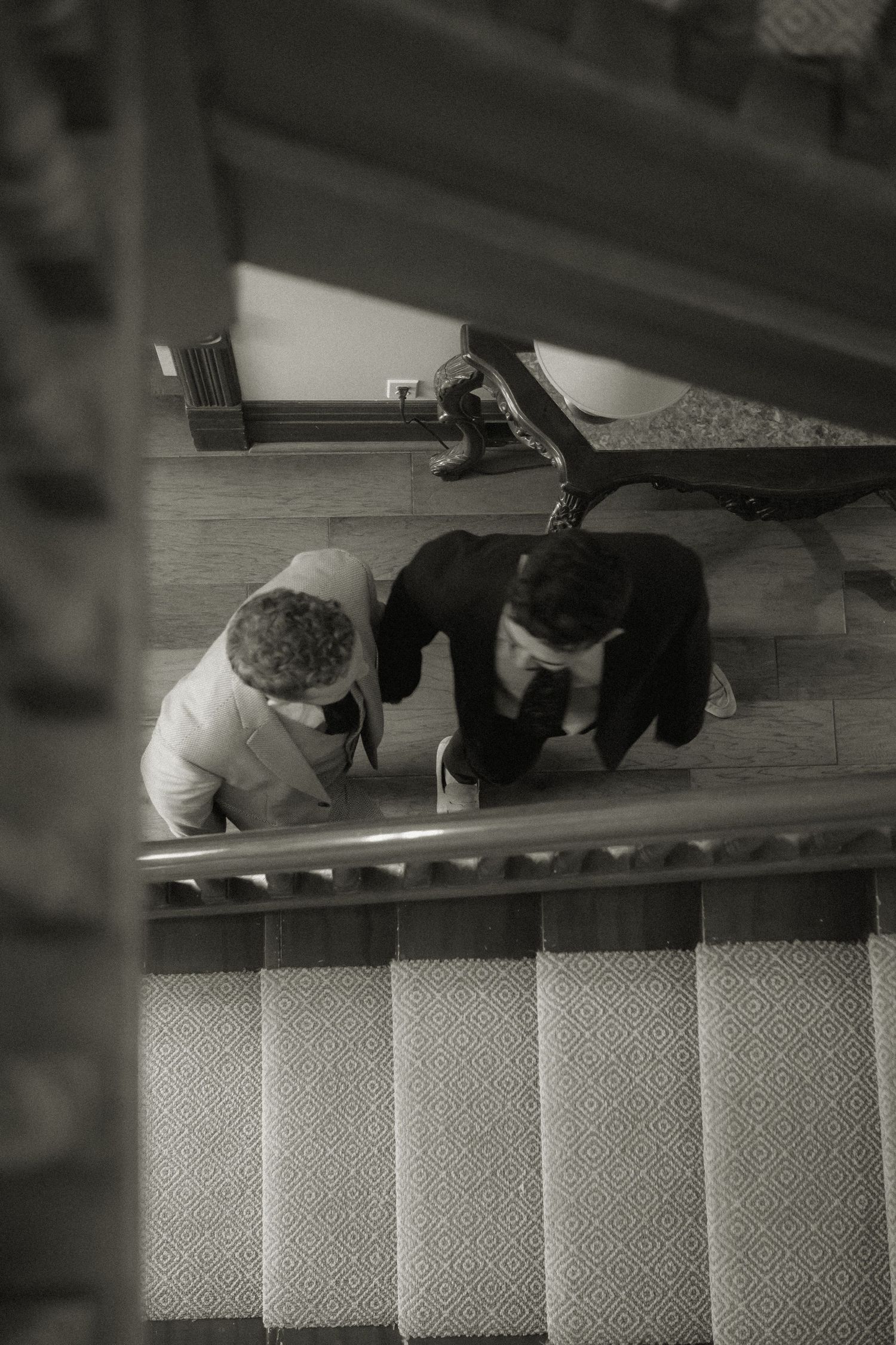Black and white photo of two people looking down staircase.