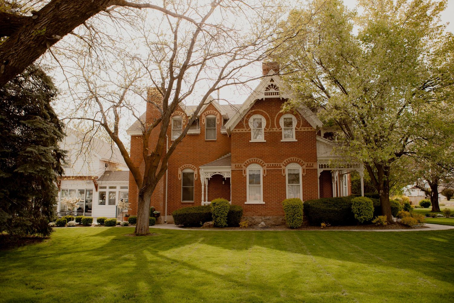 Red brick Gothic Revival style house with white trim and landscaped lawn on a sunny day.