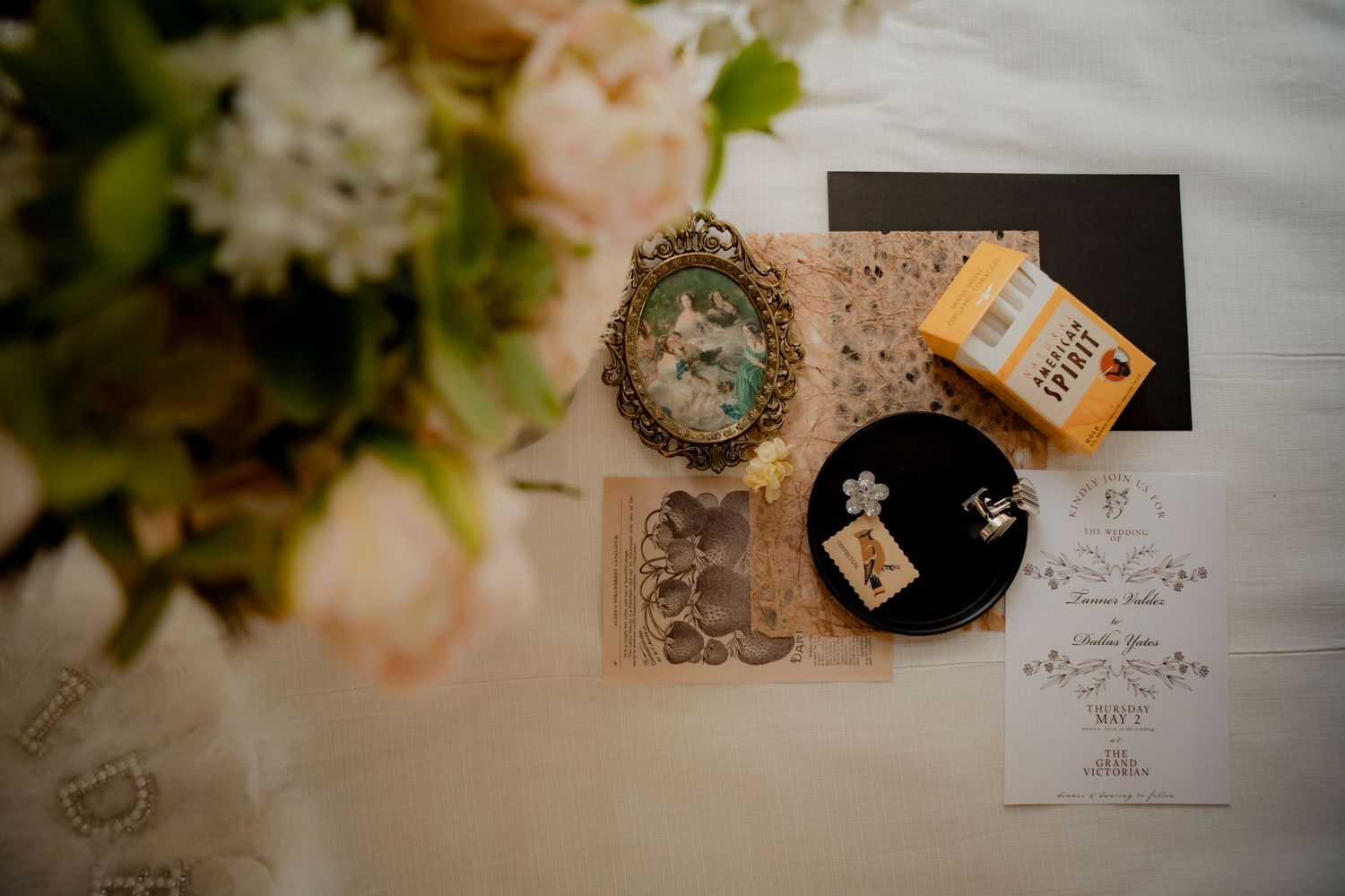 Wedding detail flatlay with floral arrangements, vintage decor, and paper elements on white surface.
