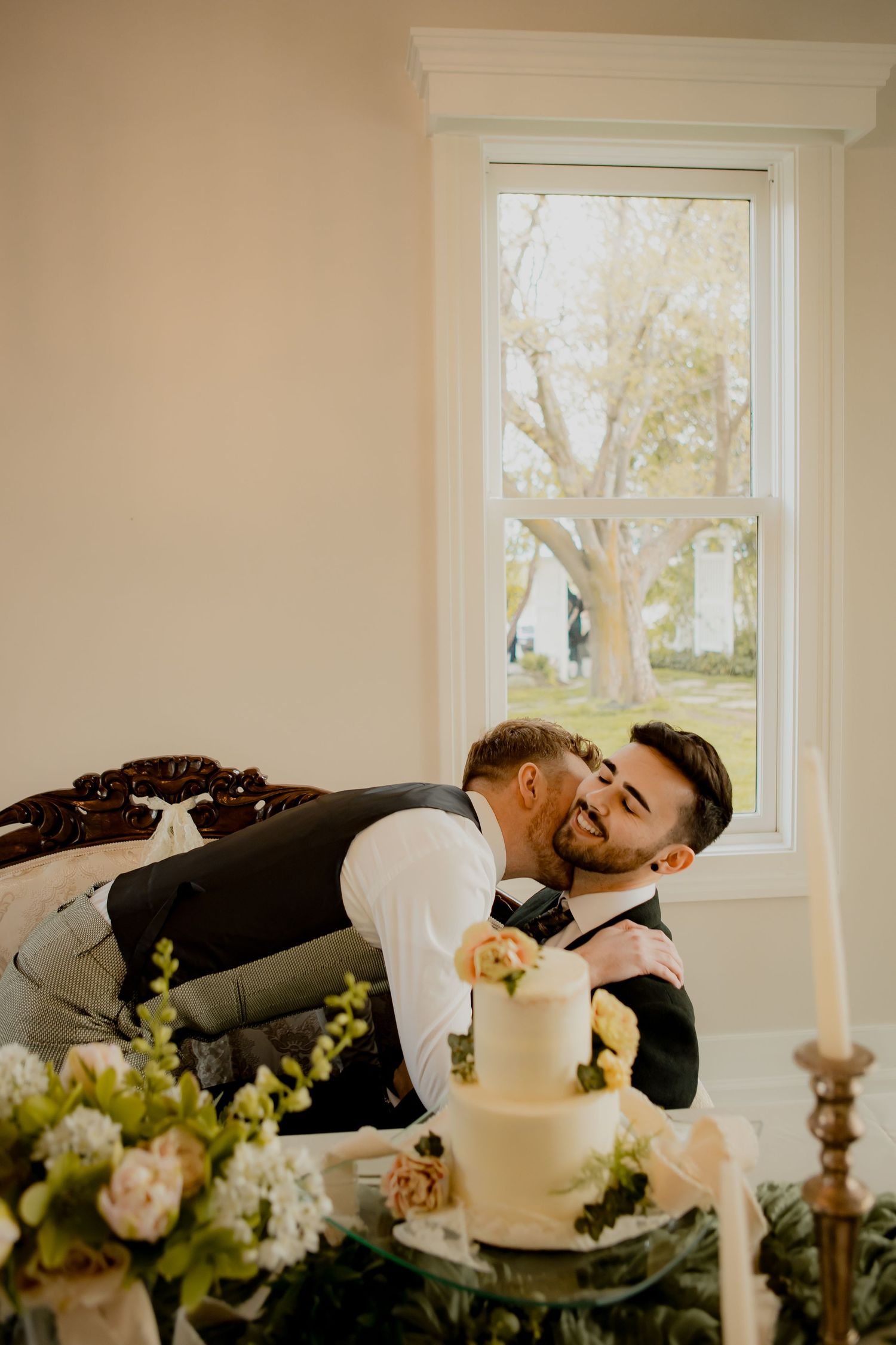 Two people leaning over a wedding cake with candlelight and floral decorations.