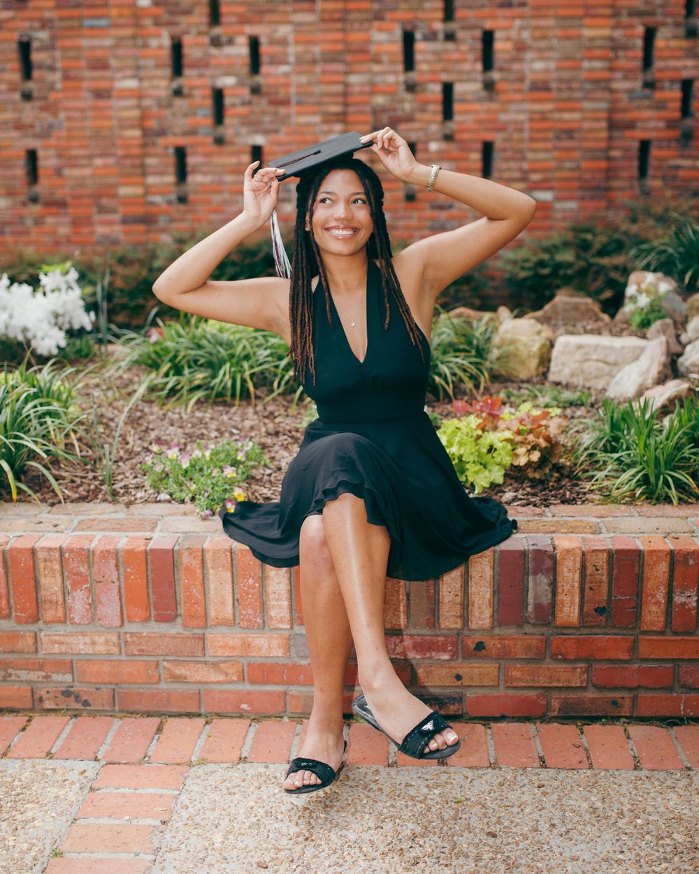A celebratory graduation photo on brick steps with someone adjusting their mortarboard cap.