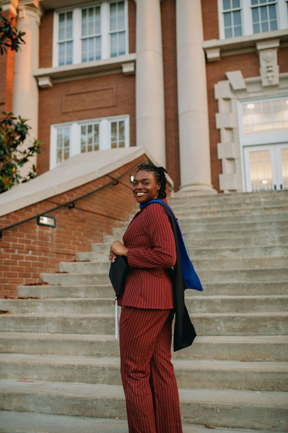Smiling woman in red pinstripe suit poses on steps outside a brick building.