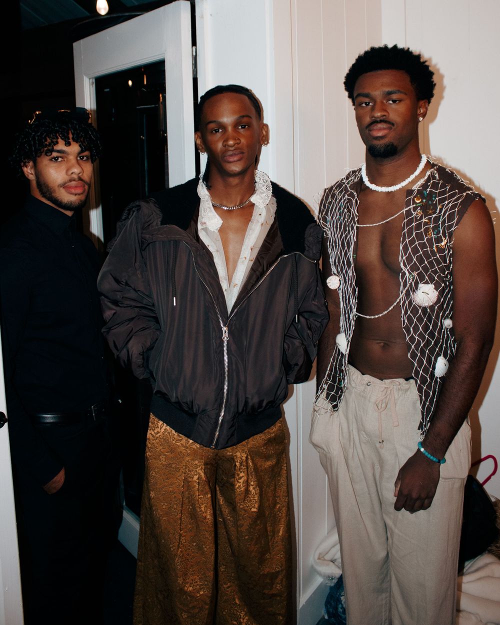 Three models pose together at a fashion event wearing stylish casual and avant-garde outfits.