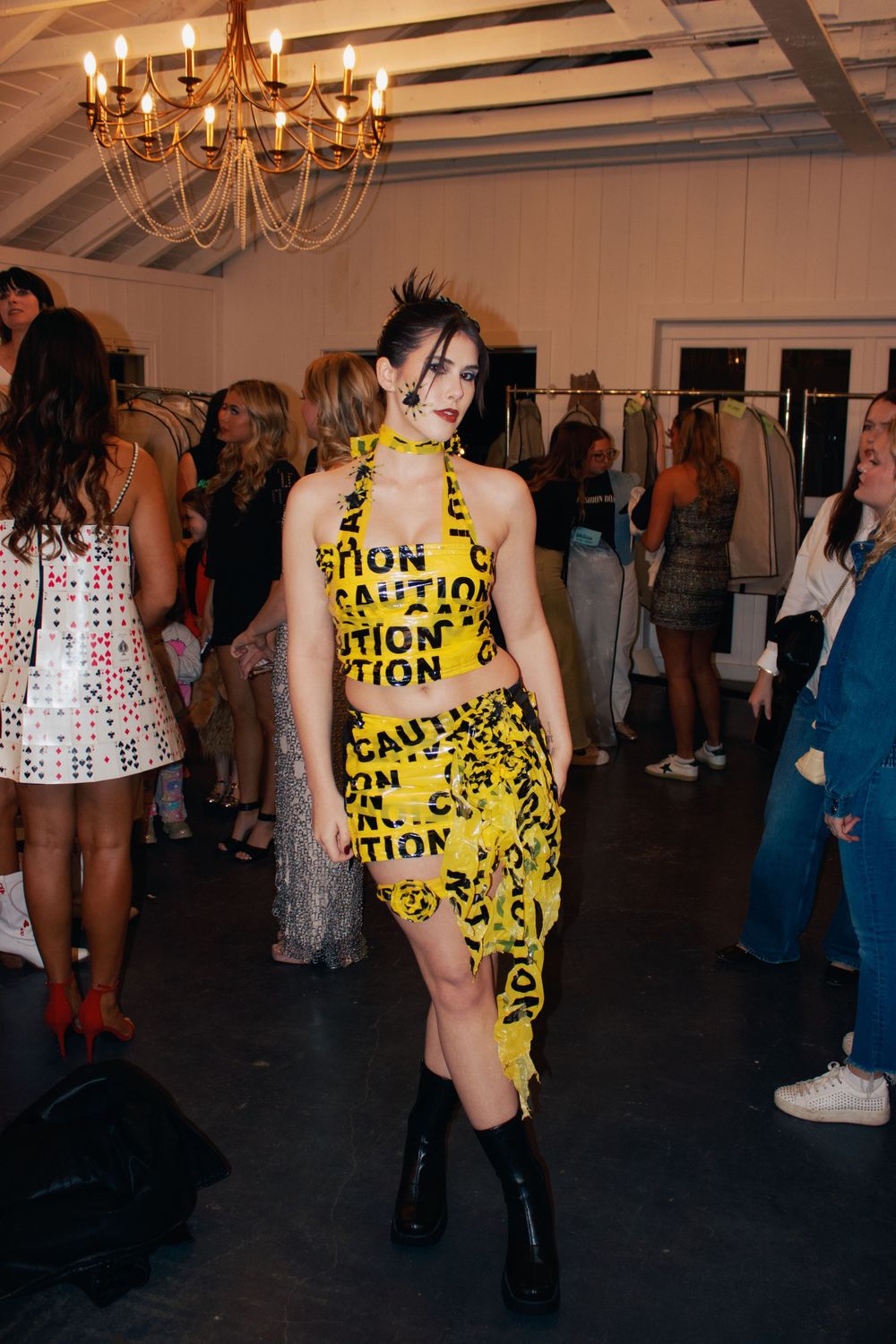 Model walks runway in yellow caution tape inspired outfit with black boots.