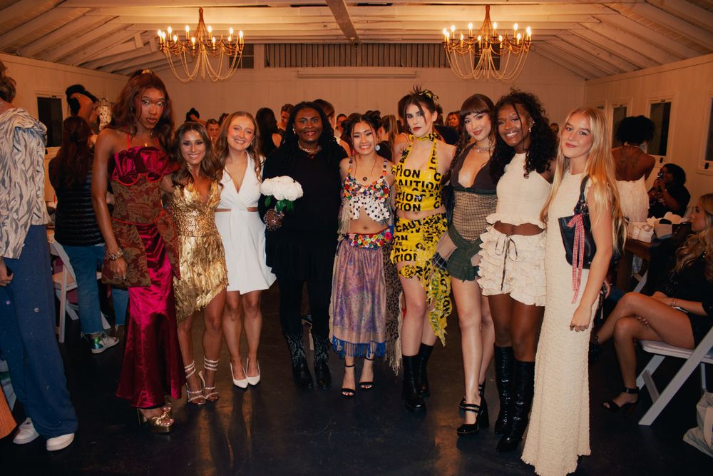 Group photo of fashion show participants posing together under chandelier lighting.