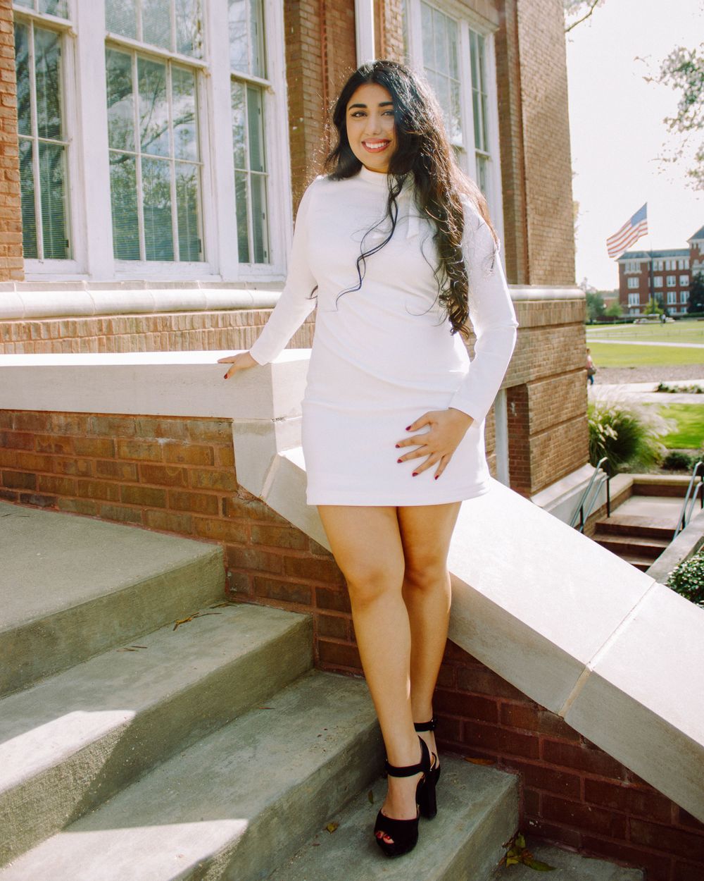 Portrait series against brick building wearing white sweater and black boots on concrete steps.
