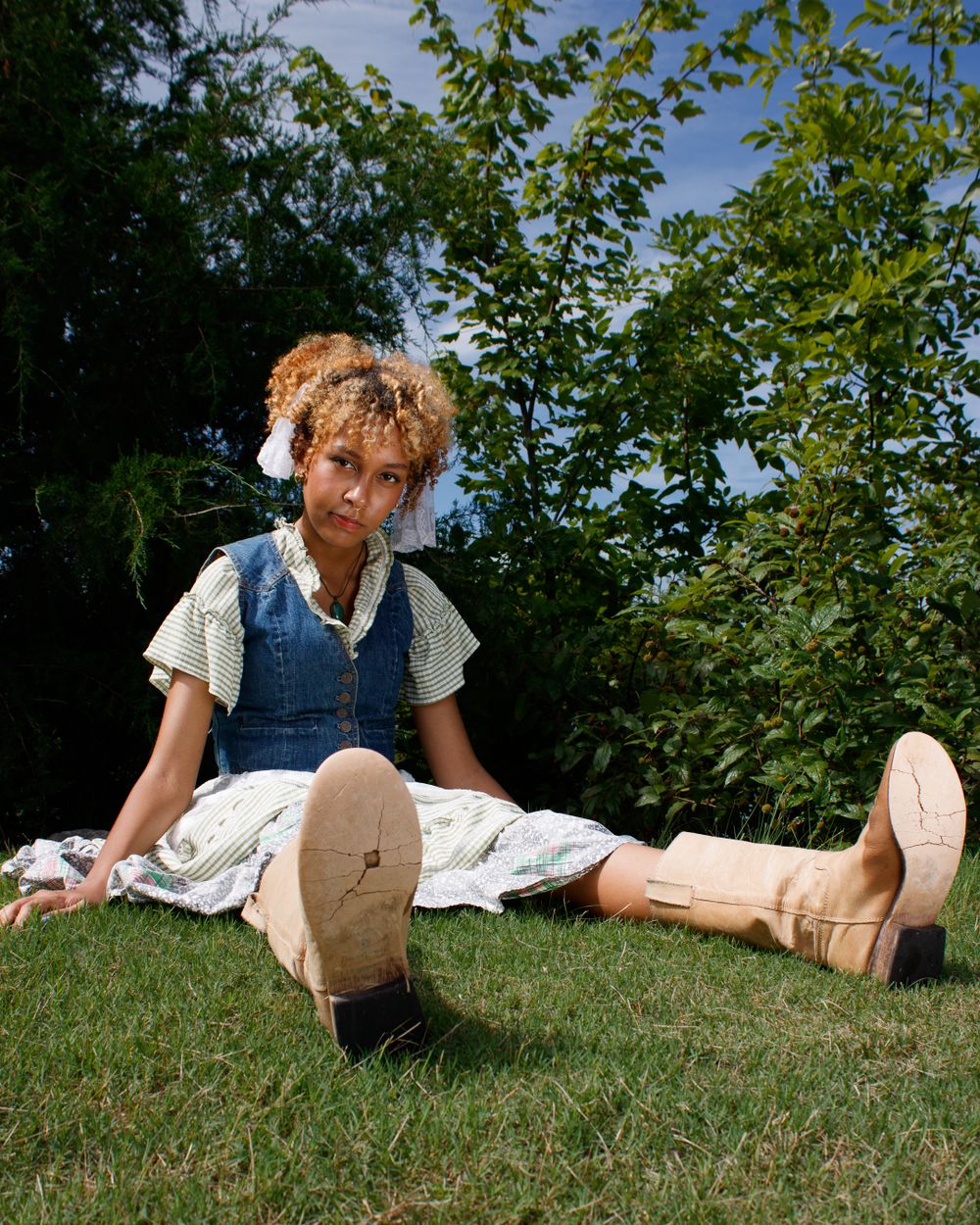 Casual summer fashion shot with model sitting on grass wearing denim and white dress combination.